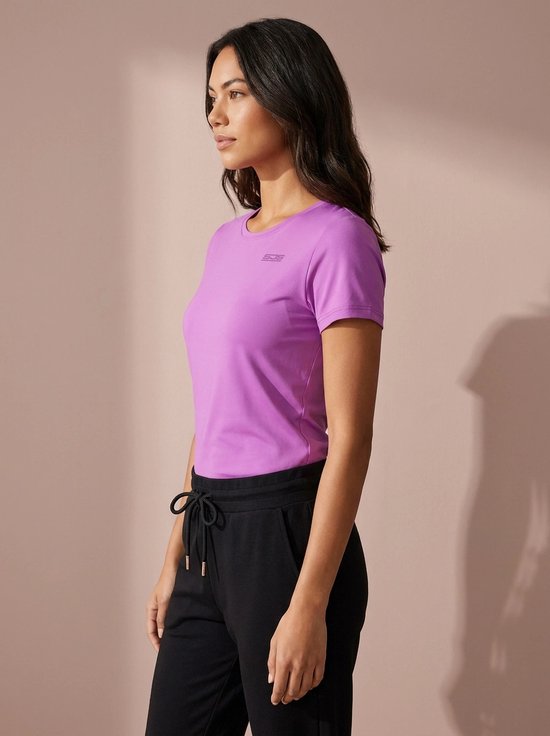 Vrouw in paars sportshirt met korte mouwen, SJG logo op de borst en zwarte sportbroek.
