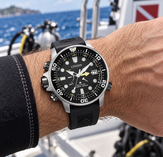 Zwart Citizen Eco-Drive duikhorloge met zilverkleurige kast, gedragen om pols. Zwarte band met profiel.