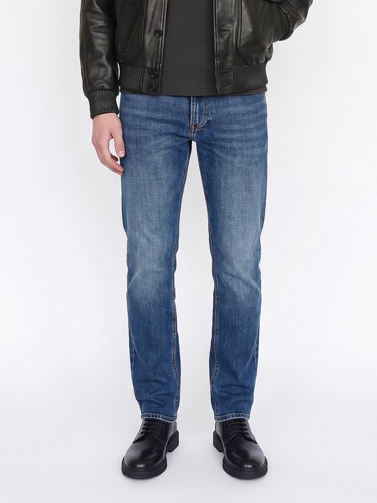 Close-up van een blauwe jeans gecombineerd met een zwarte leren jas en zwarte schoenen.