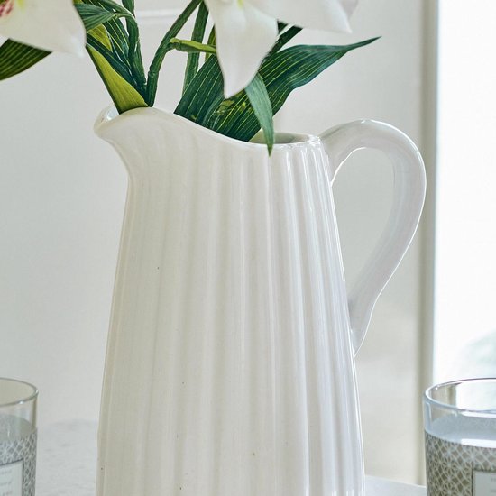 Witte karaf met verticale ribbels, met witte lelies in een vaas.