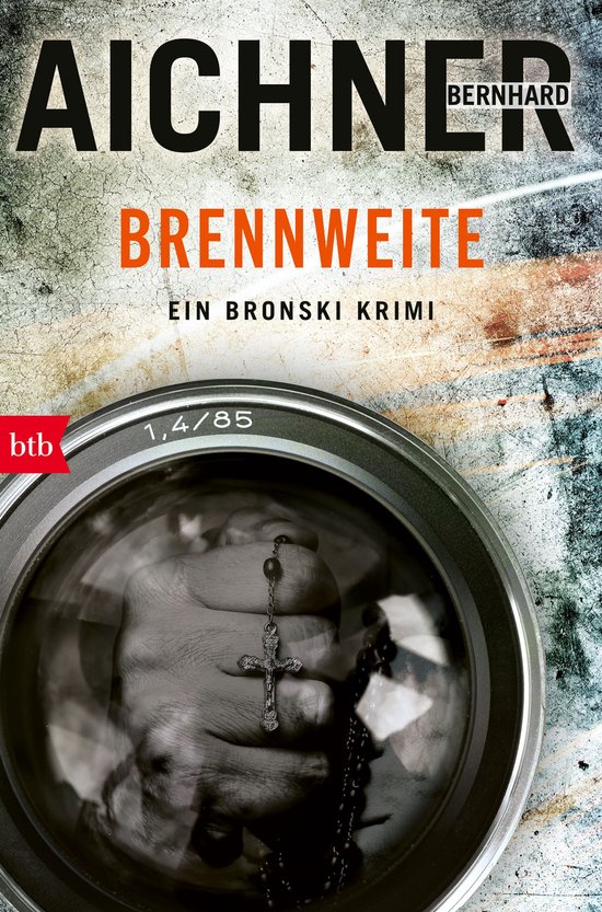 Boekomslag met de titel "BRENNWEITE" en "EIN BRONSKI KRIMI". Een gesloten hand met een kruisje wordt vergroot weergegeven door een cameralens.