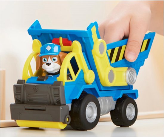 Kind handen bedienen een blauwe kiepwagen met gele onderdelen, hondje zit erin.