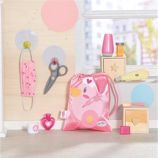Op een witte plank liggen een masker, een schaar, een roze tas, een flesje en een thermometer.