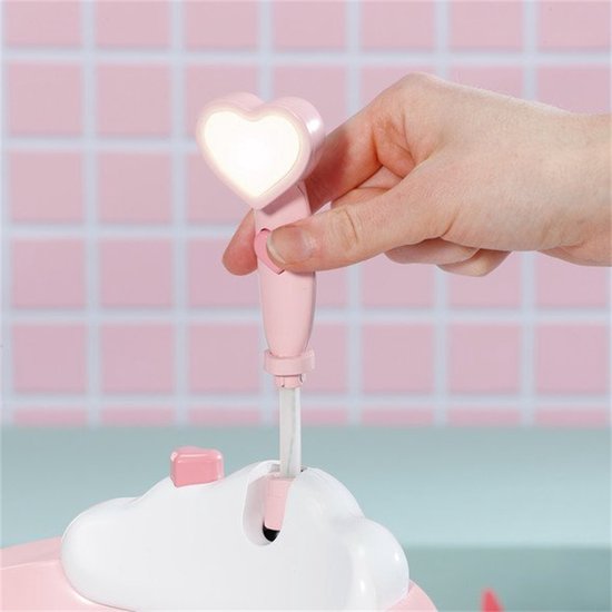 Hand houdt roze douchekop met hartvormige lamp vast, die oplicht en water sproeit.