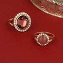 Twee gouden ringen met ronde, donkerrode en roze stenen, omringd door zirkonia's.