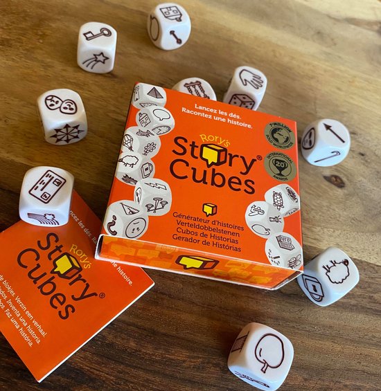 Rory's Story Cubes doos en losse dobbelstenen op een houten tafel. Dobbelstenen hebben afbeeldingen van een sleutel, huis, hand, schaap en boom.