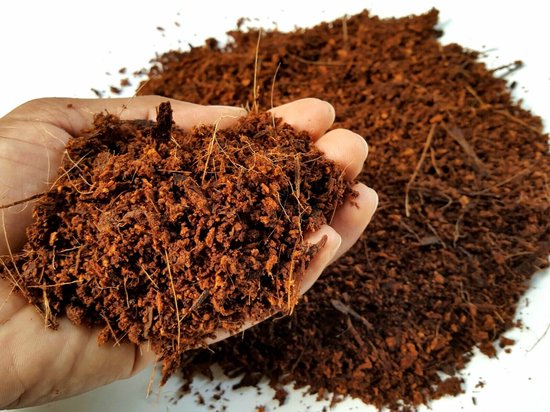Hand vol bruin kokosgrind met droge vezels en een hoopje erachter.