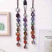 Drie chakra hangers met veelkleurige ruwe edelstenen zoals amethist en rode jaspis, gevlochten met bruin touw, hangend aan een witte muur.