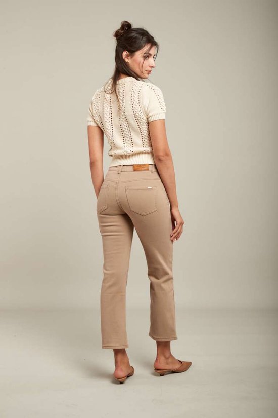 Achterkant model in crème gebreide top met korte mouwen en beige jeans. De jeans hebben een bruin leren label.