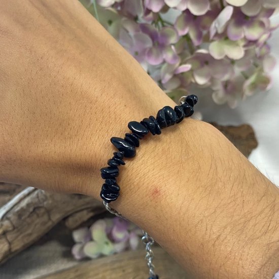 Zilverkleurig schakelarmbandje met ruwe zwarte steentjes, gedragen om een pols.