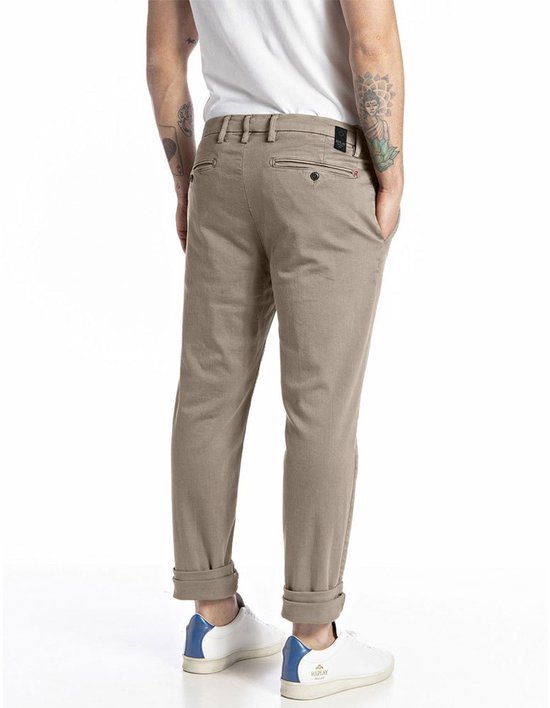 Achterkant van een beige chino met opgerolde broekspijpen en witte sneakers.