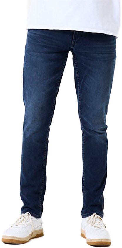 Detail van een donkerblauwe slim fit jeans met lichte wassing, gedragen door een man.