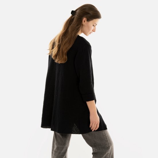 Model van achteren gezien, draagt een lang, zwart gebreid vest.