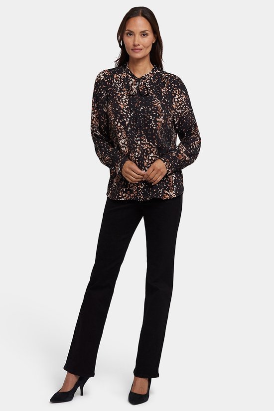 Model draagt een zwart strik-hals blouse met bruine en beige vlekkenprint en zwarte broek.
