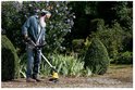 Een oudere man met baard en koptelefoon gebruikt de Kärcher onkruidverwijderaar in de tuin.