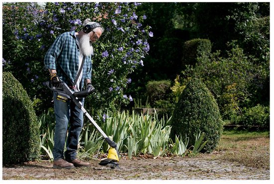 Een oudere man met baard en koptelefoon gebruikt de Kärcher onkruidverwijderaar in de tuin.