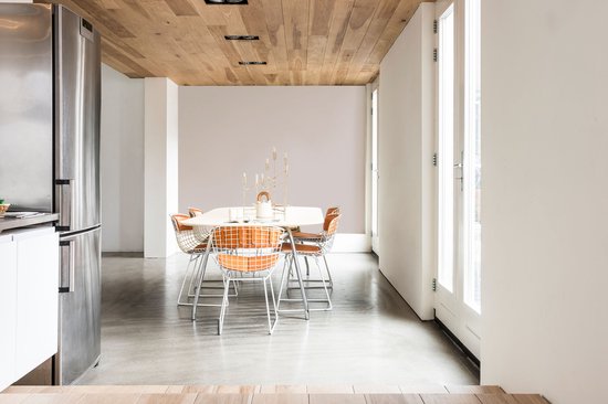 Een eetkamer met een tafel en zes oranje stoelen, naast een roestvrijstalen koelkast en glazen deuren.