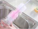 Een hand gebruikt een roze en witte flesborstel om een glazen fles schoon te maken in een gootsteen.