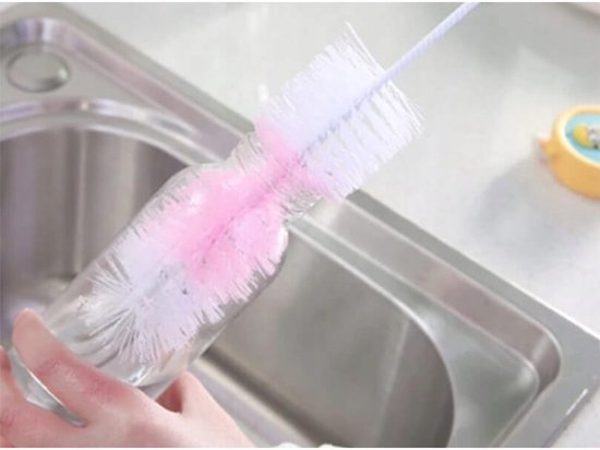Een hand gebruikt een roze en witte flesborstel om een glazen fles schoon te maken in een gootsteen.