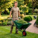 Man met tuingereedschap in groene opvouwbare kruiwagen in de tuin.