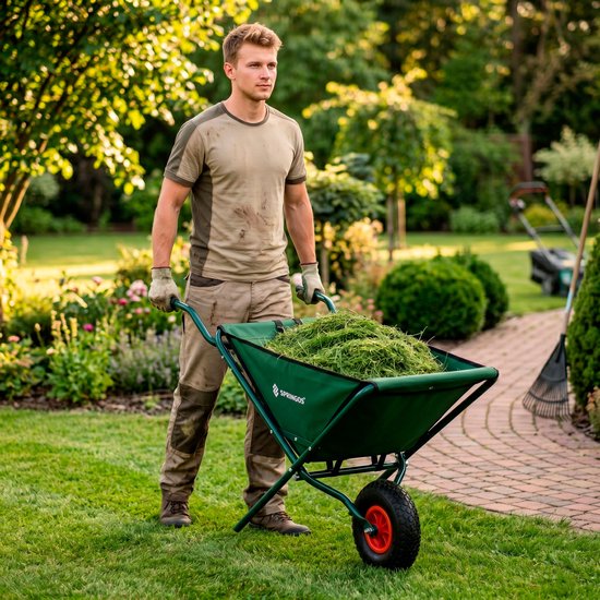Man met tuingereedschap in groene opvouwbare kruiwagen in de tuin.
