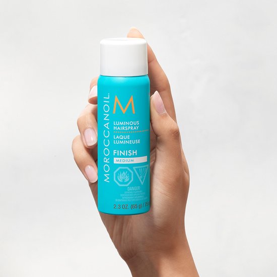 Hand met Moroccanoil Luminous Hairspray Medium, turkooizen spuitbus met oranje M-logo. 75 ml.
