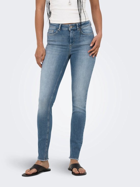 Model met de handen in de zakken, draagt een blauwe skinny fit jeans met middelhoge taille en rafels aan de zoom.