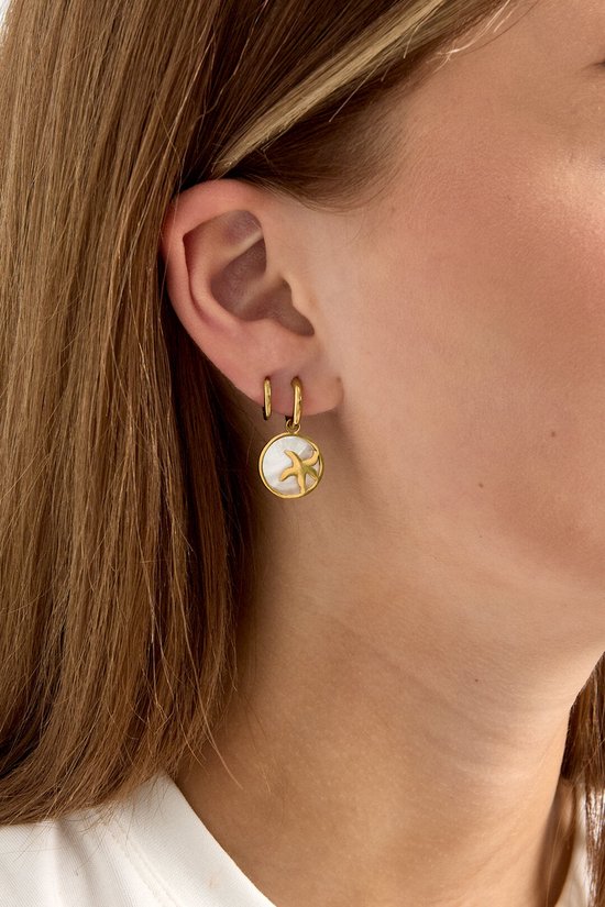 Gouden oorbel met een ronde witte hanger en een zeester.