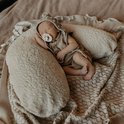 Pasgeboren baby slaapt op een beige voedingskussen, draagt een beige romper en mutsje met pompon.