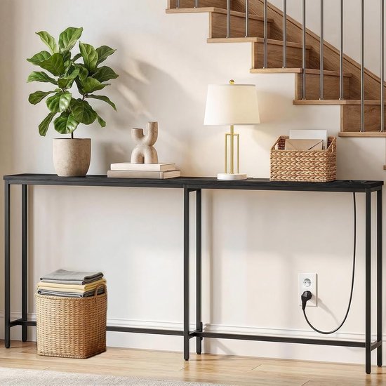Zwarte consoletafel achter een bank, met plant, lamp, boeken, mand en opgeladen telefoon.