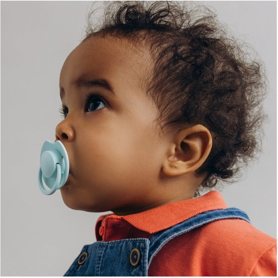 Een baby met donker haar en een oranje shirt draagt een lichtgroene LOVI fopspeen.