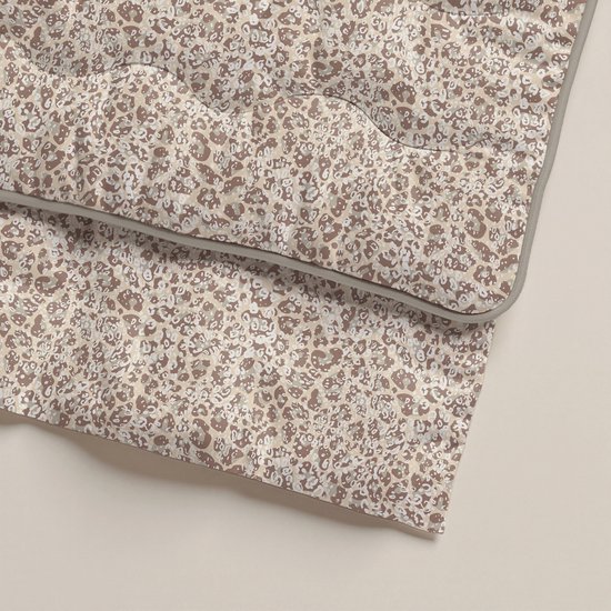 Detail van een gevouwen dekbed met zandkleurige panterprint en grijze rand.