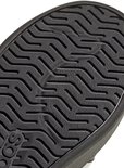 Detail van de zwarte, golvende loopzool van een Adidas-sneaker met het Adidas-logo.