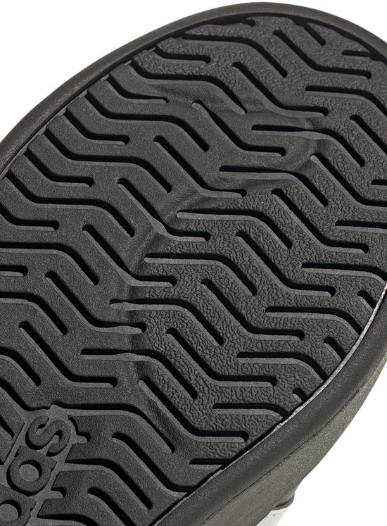 Detail van de zwarte, golvende loopzool van een Adidas-sneaker met het Adidas-logo.