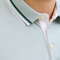 Close-up van de kraag en knoopsluiting van een lichtblauwe poloshirt met textuur en contrasterende strepen.