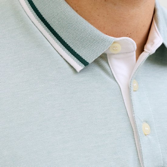Close-up van de kraag en knoopsluiting van een lichtblauwe poloshirt met textuur en contrasterende strepen.
