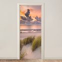 Deurposter met duinlandschap bij zonsondergang boven de zee.
