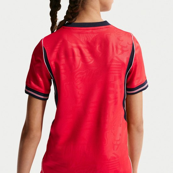 Achterkant van een rood voetbalshirt met navy blauwe zijkanten en witte biezen. Het shirt heeft een subtiel patroon.