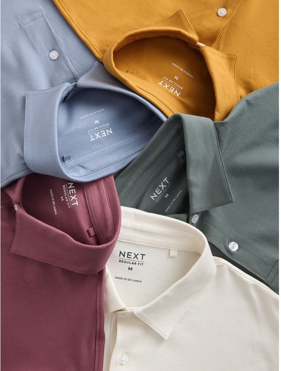Een stapel poloshirts in de kleuren grijsblauw, mosterdgeel, donkergroen, bordeauxrood en crème. De kraag en het label met 'NEXT REGULAR FIT' zijn zichtbaar.