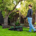 Vrouw maait gras met groene Bosch grasmaaier in een tuin met boom.