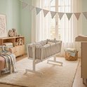 Witte wieg met grijze ruitjes bekleding in een kinderkamer met een roze stoel en een slinger.