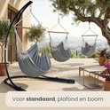 Grijze hangstoelen aan een standaard, plafond en boom, met uitzicht op de bergen.