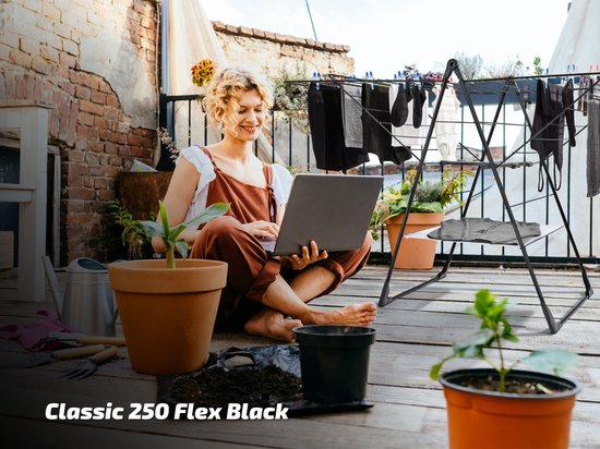 Zwarte vrouw werkt op laptop op balkon, met zwart Classic 250 Flex droogrek vol wasgoed.