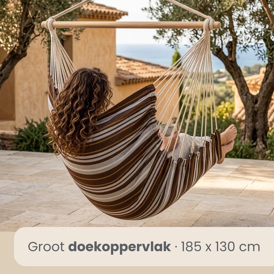 Vrouw met krullend haar in een gestreepte hangstoel, zittend op een terras met uitzicht op de zee.