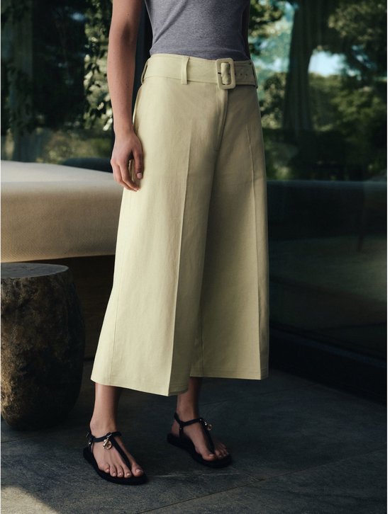 Model draagt een lichtgroene culotte met een riem en een grijs vest.