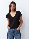 Model met handen in de zakken van een jeans, draagt een zwart T-shirt met V-hals.
