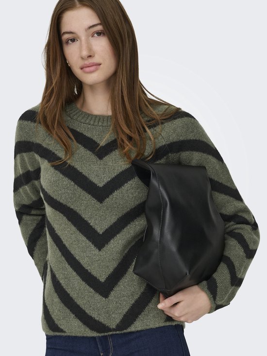 Model draagt een groene trui met zwarte chevron-strepen en donkere jeans, vasthoudend aan een zwarte tas.