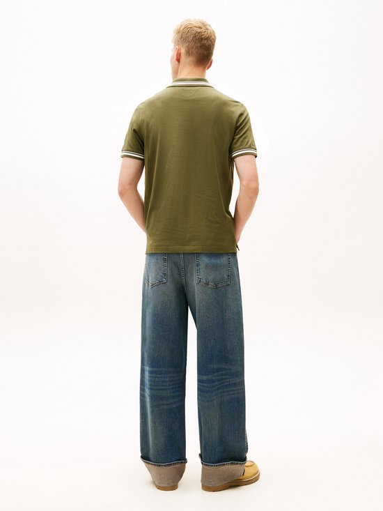 Zijaanzicht van een man met blond haar die een olijfgroene polo en jeans draagt.