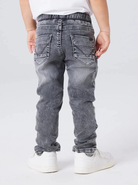 Achterkant van een jongetje in grijze jeans en witte sneakers, met gedetailleerde achterzakken.