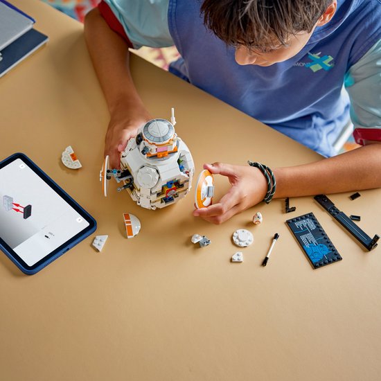 Un garçon construit un BB-8 LEGO sur une table, avec une tablette et des pièces.